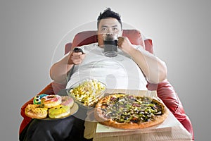 Obese man drinking and overeating on the sofa