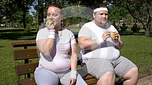 Obese man eating burger, fat girl admiring apple, choice of junk or healthy food