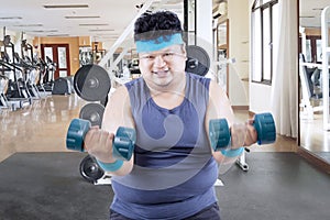 Obese man exercising with barbells in gym center
