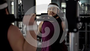 Obese man hardly doing exercise with barbell in gym, fitness workout, sport