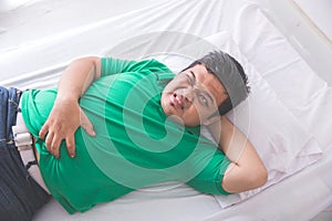 Obese man having stomach ache while laying on a bed