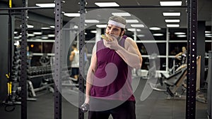 Obese man holding dumbbell eating burger, refusing from doing sport, addiction