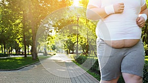 Obese man jogging in park, persistent in losing weight, big belly close up