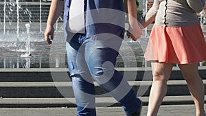 Obese man and lady walking together in city holding hands, romantic outdoor date