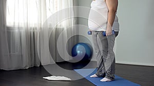 Obese man lifting dumbbells, working out at home, burning calories, motivation