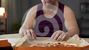 Obese man looking at fatty pizza on table, junk food addiction, overeating