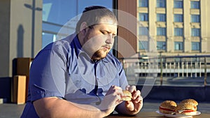 Obese man looking at hamburger, hesitating to eat, choosing healthy lifestyle