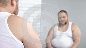 Obese man looking at his mirror reflection, overweight problem and insecurities