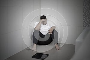 Obese man looks unhappy with a scale in bathroom