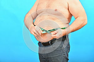 An obese man measures his big belly with a centimeter