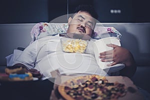 Obese man sleeping with junk foods on the bed