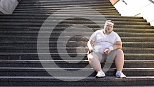 Obese man in sportswear sitting on stairs, lack of motivation for weight loss