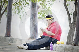 Obese man using phone after exercises in the park