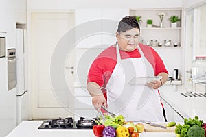 Obese man using a tablet and preparing salad