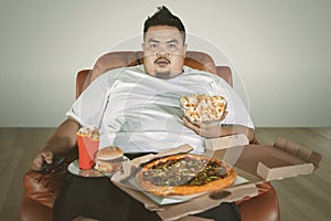 Obese man watching TV with junk foods at home