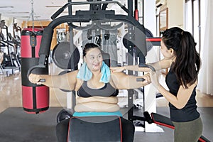 Obese woman assisted by her trainer to workout