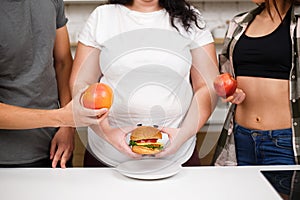 Obese woman with burger and fit people with fruits