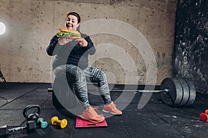 Obese woman combining sport and junk food, fat girl having snack during workout