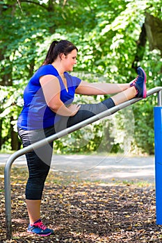 Obese woman doing sport stretching outdoors in park