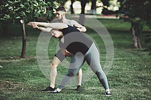 Obese woman doing stretching exercise with trainer