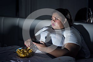 Obese woman eating popcorn in bed