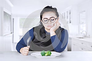 Obese woman feeling bored with broccoli