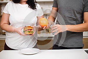 Obese woman with hamburger and trainer with fruits