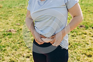 Obese woman hand holding excessive belly fat over nature background. Diet concept to reduce belly and shape up healthy