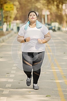 Obese woman jogging on the road at autumn time