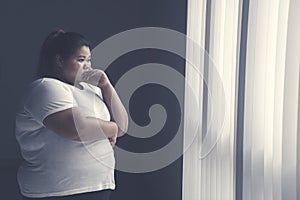 Obese woman looks pensive near the window