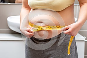Obese woman measuring her waist at the bathroom
