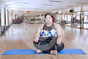 Obese woman meditating in the fitness center