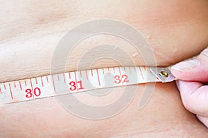 Obese woman with operation scar measuring her waist with a tape measure. Loosing fat after operation. Healthy lifestyle. Diet