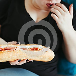 Obese woman sitting on sofa eating unhealthy food