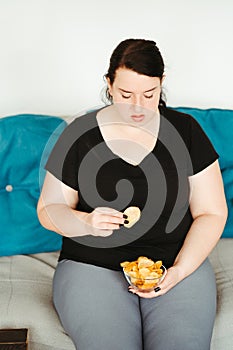 Obese woman sitting on sofa eating unhealthy food
