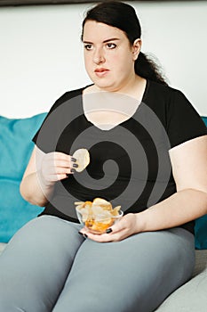 Obese woman sitting on sofa eating unhealthy food