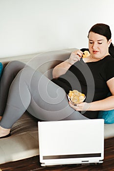 Obese woman sitting on sofa eating unhealthy food