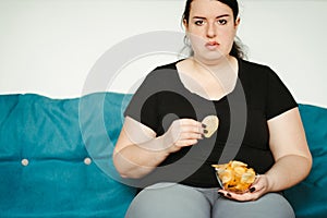 Obese woman sitting on sofa eating unhealthy food