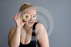 Obese Woman in sports clothes closes one eye with a donut