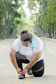 Obese woman tying her shoelaces on the road