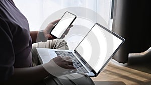 Obese woman working with laptop computer and using smart phone while sitting on wooden floor.