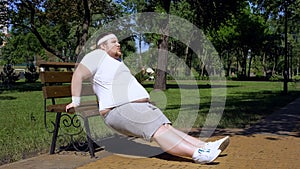 Obese young man exercising on bench, outdoor workouts, struggle to slim down