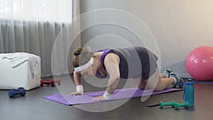 Obese young woman pushing up and falling on floor, working hard to lose weight