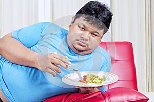 Obesity man hating to eats healthy salad at home