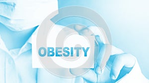 Obesity word on card shown by a Doctor with surgical mask on his face. Weight loss eating disorders woman healthcare
