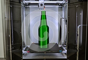 Object green bottle printed on 3D printer close-up, on desktop of 3d printer.