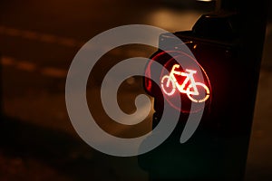 oblique closeup view on traffic light for a cycling lane showing red bicycle symbol at night with car lights in background