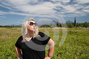 Obnoxious blonde woman does a duck face with pouting lips, hands on hips, in Glacier National Park, near Polebridge, Montana, in a photo