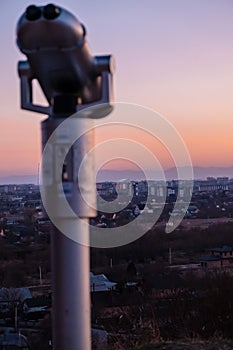 Observation deck and binoculars with a view of the city. Coin operated telescope binocular for sightseeing. Sunset above the city