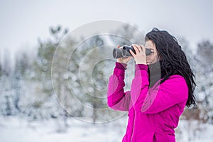 Observation of nature in the winter season. Travel concept, girl looks through binocularsb. Woman in winter forest with